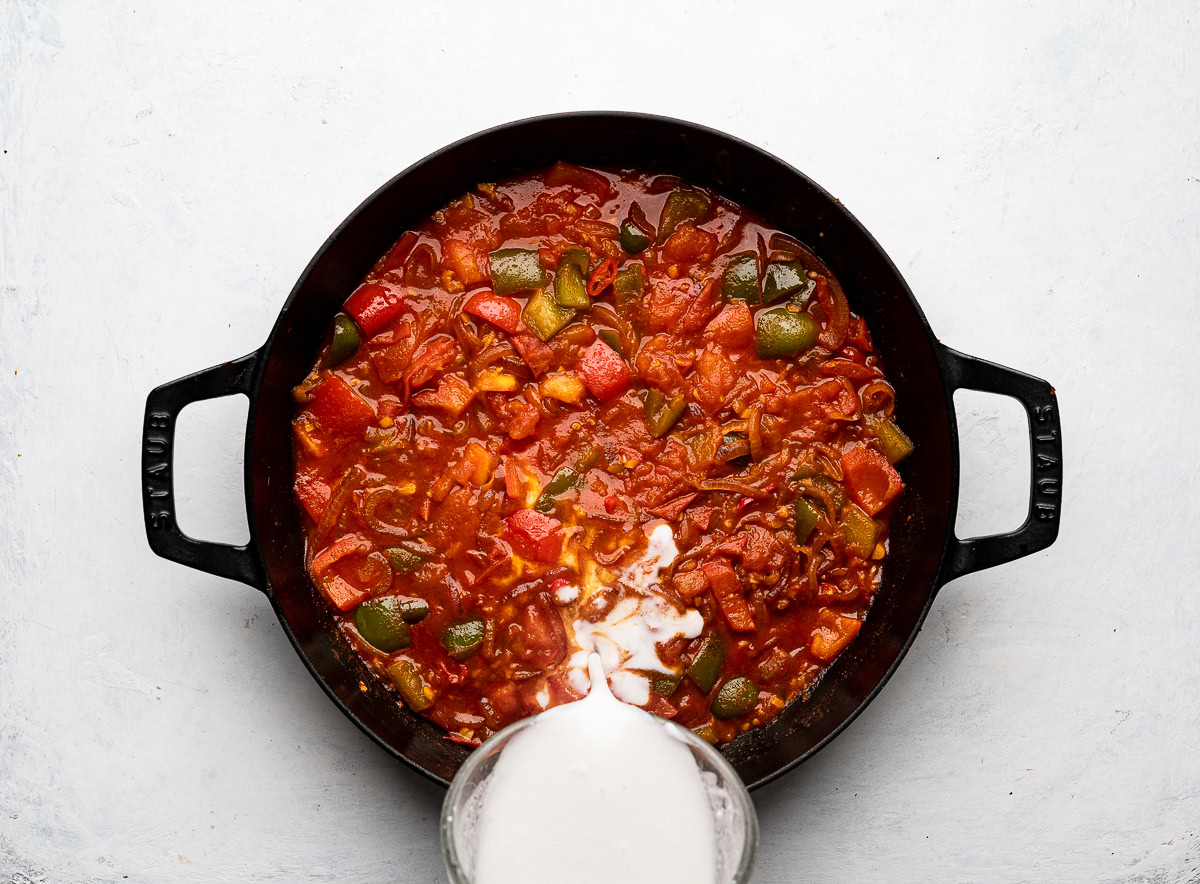 pouring coconut milk into tomato and vegetable mixture