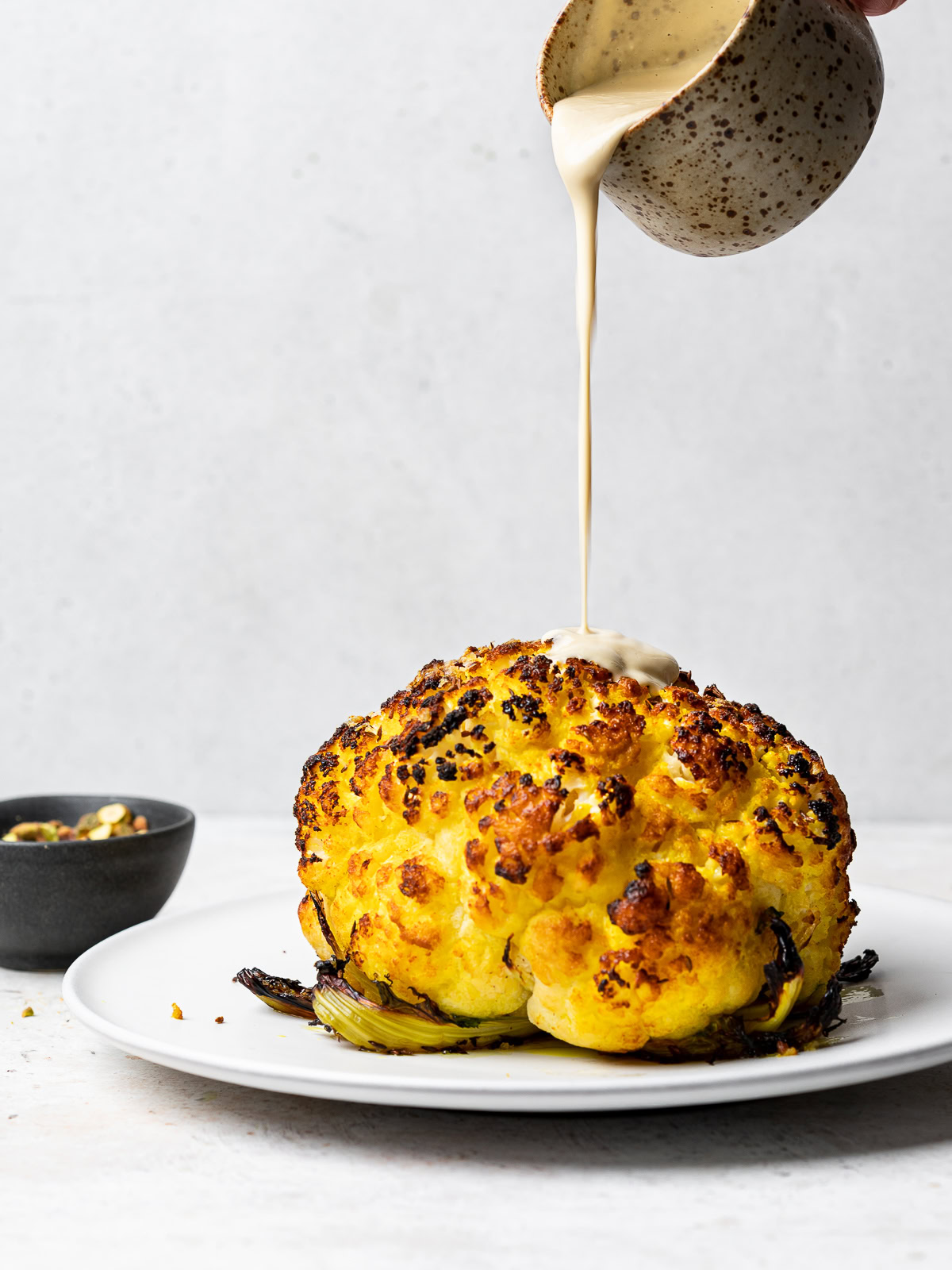 side-view of roasted cauliflower getting drizzled with tahini sauce