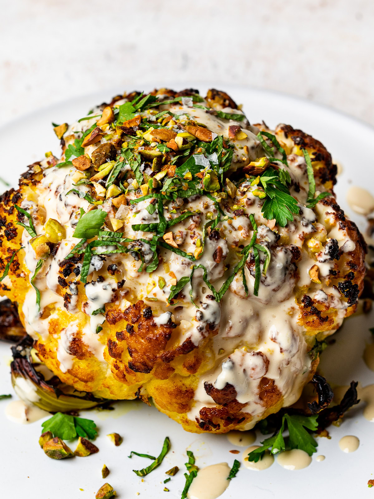 close up of cauliflower drizzled with tahini sauce and garnished with herbs and nuts