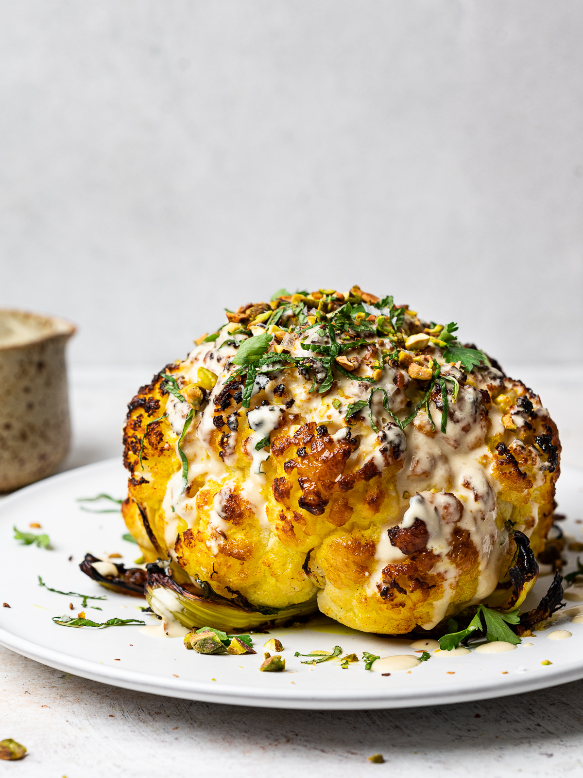 Whole roasted cauliflower drizzled with tahini sauce, fresh herbs and pistachios