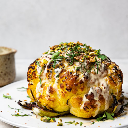 Whole roasted cauliflower drizzled with tahini sauce, fresh herbs and pistachios