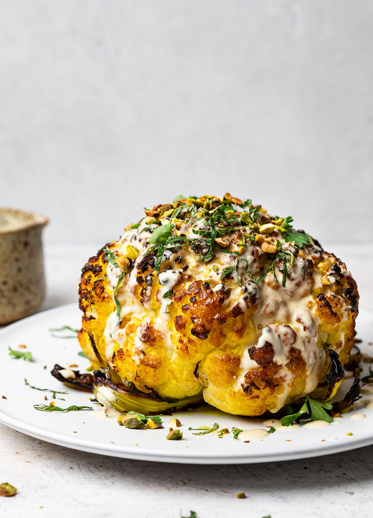 Whole roasted cauliflower drizzled with tahini sauce, fresh herbs and pistachios