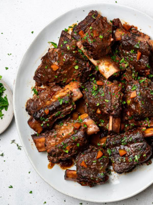 Braised short ribs served on a platter garnished with chopped parsley