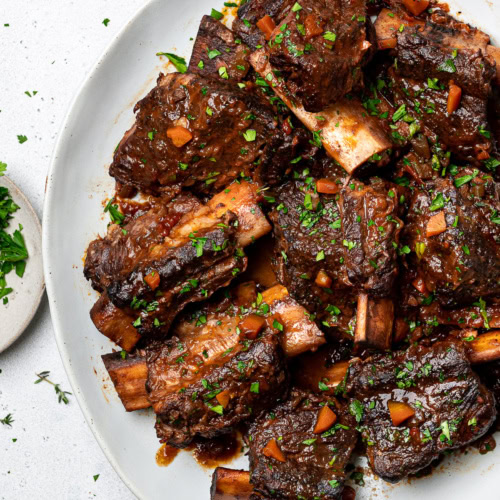 Braised short ribs served on a platter garnished with chopped parsley