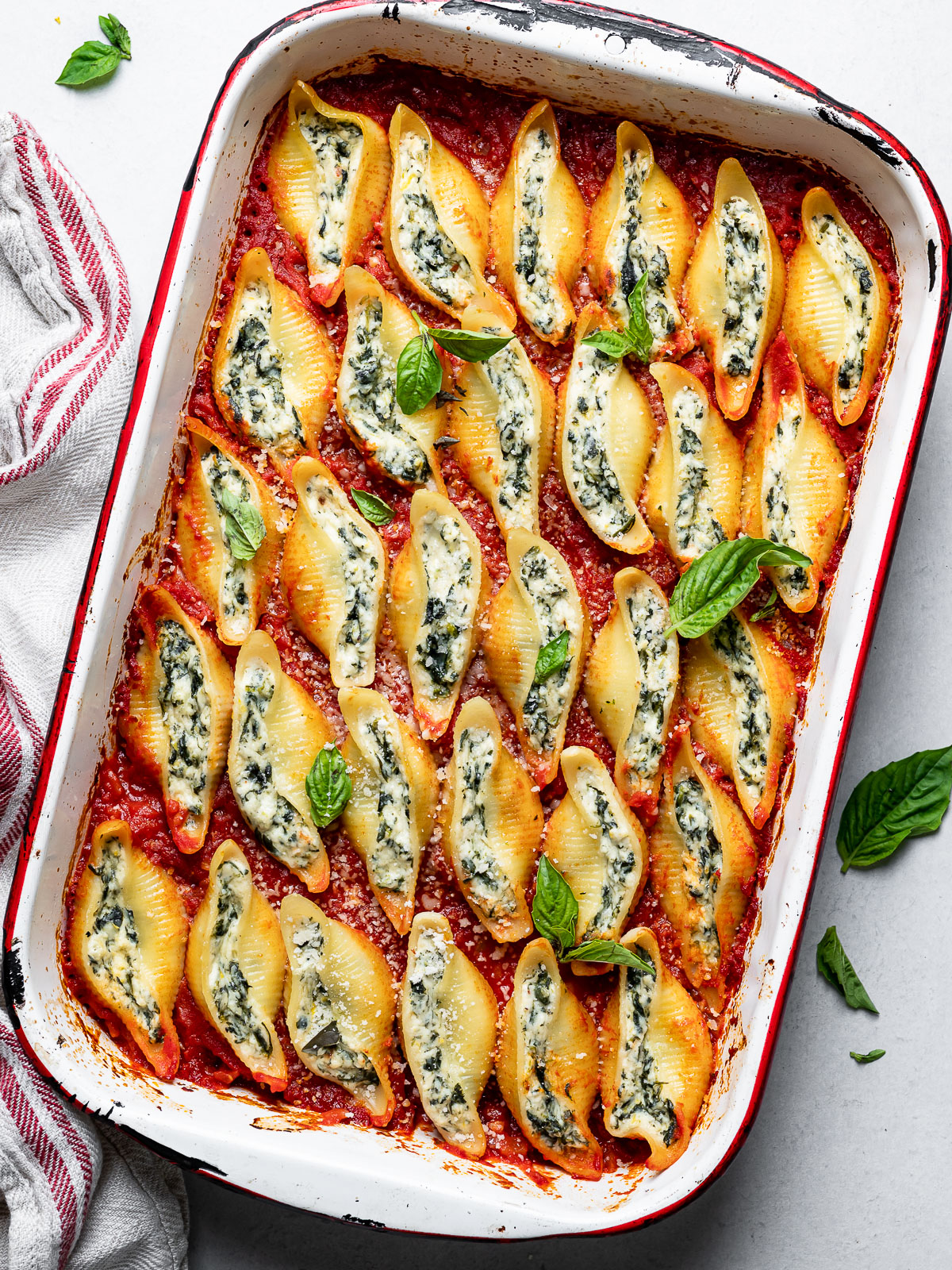 baked stuffed shells in baking dish with tomato sauce garnished with basil and parmesan cheese