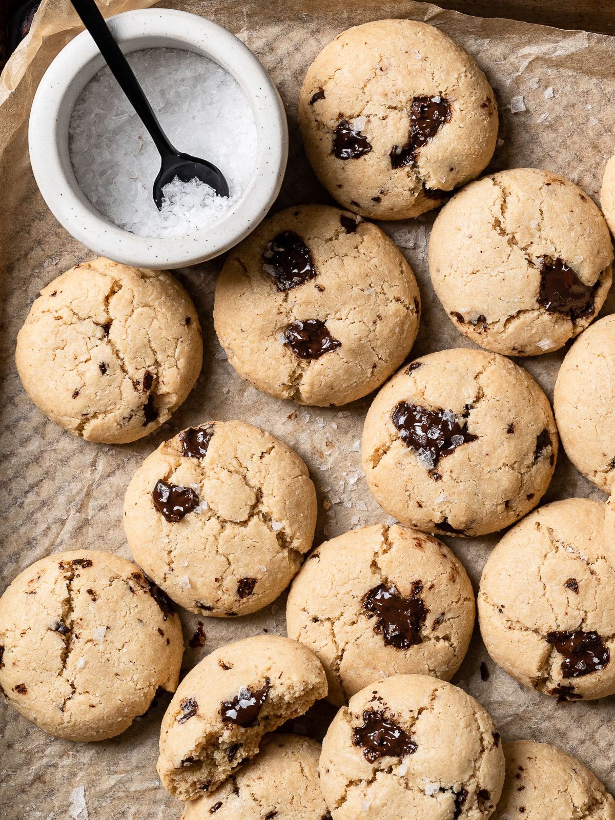 tahini cookies on baking sheet with bowl of flaky salt