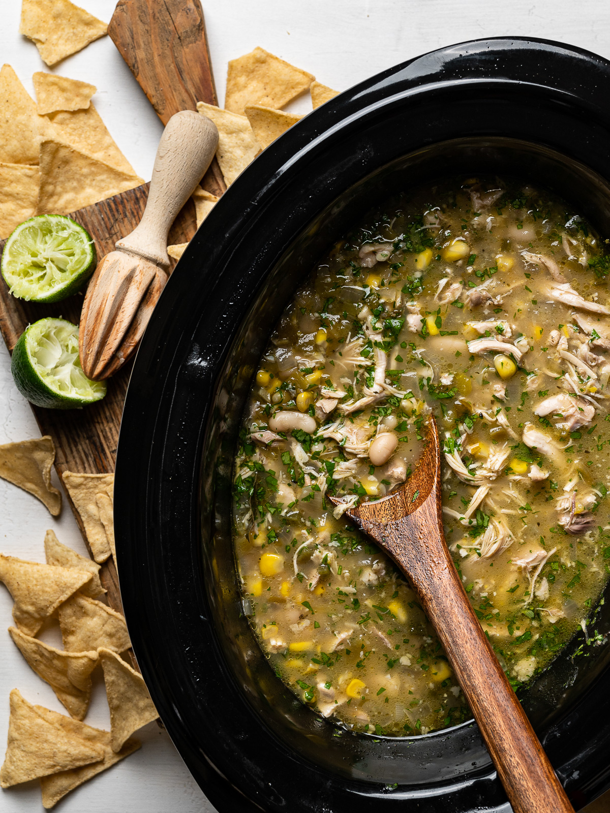 white chicken chili in slow cooker with squeezed lime wedges and tortillas scattered around
