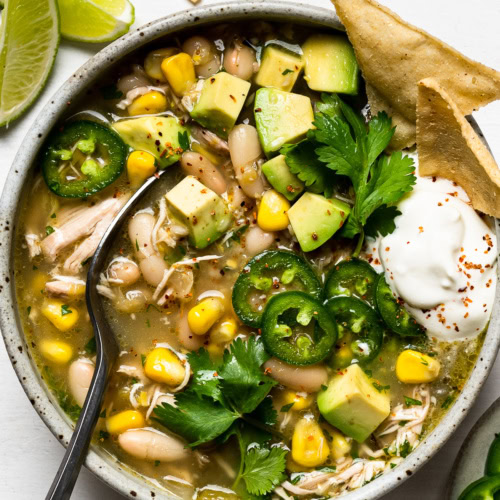 slow cooker white chicken chili served in bowl with toppings and tortillas