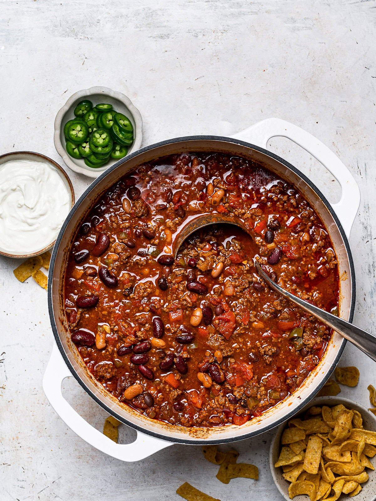 game day chili in pot with bowl of Fritos, sour cream and jalapeños on the side