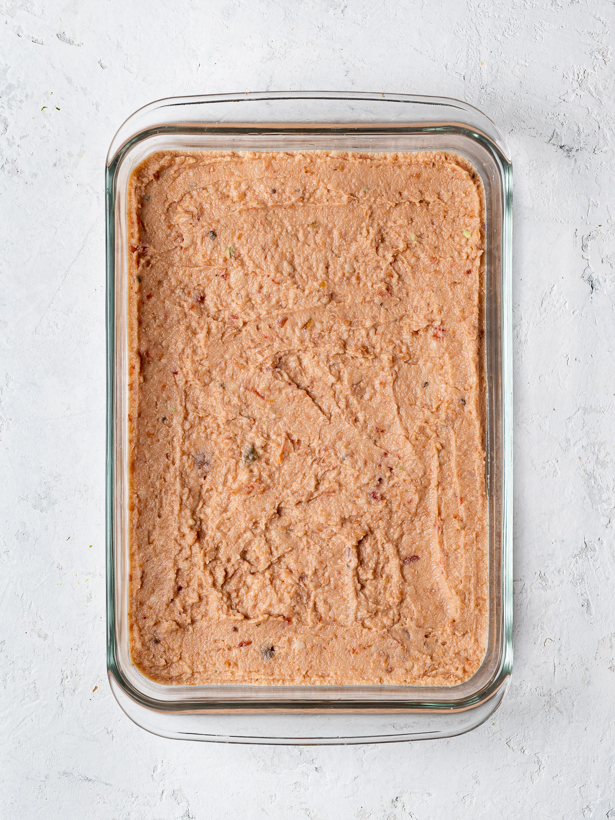 refried beans spread on bottom of glass dish