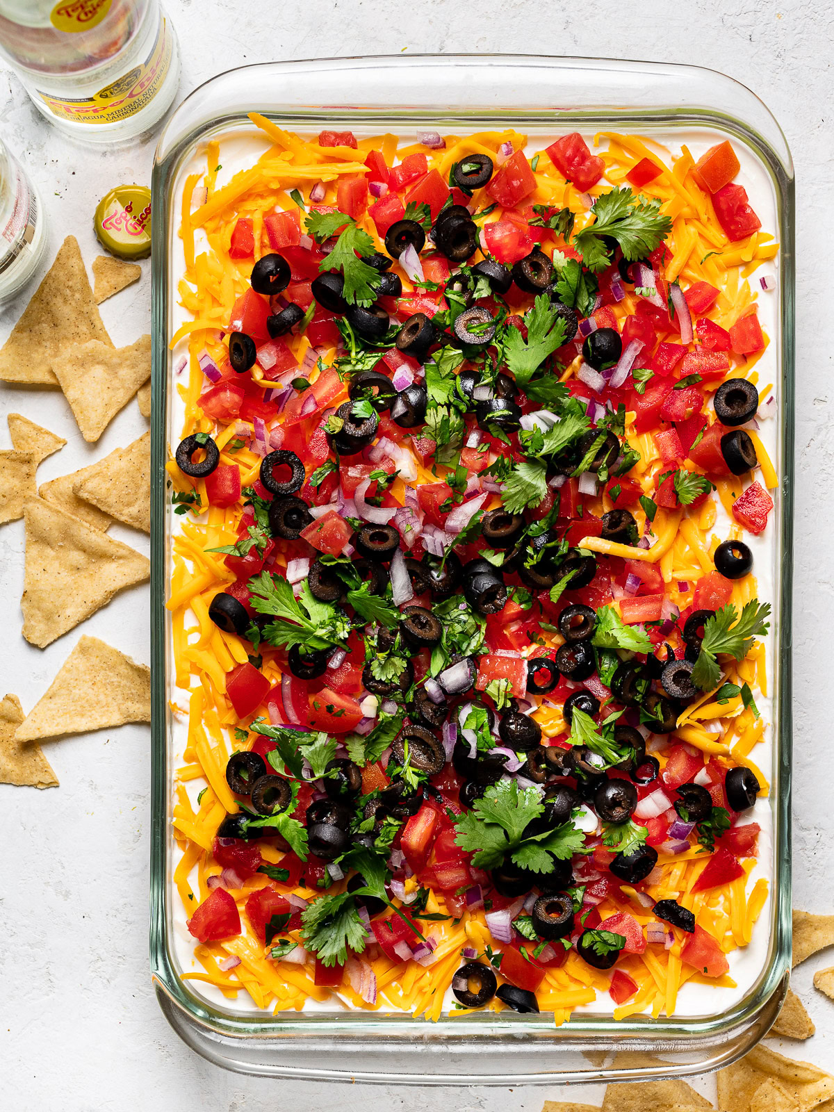 top view of 7 layer dip in glass dish with bowl of tortilla chips in the background