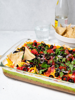 side view of 7 layer dip in glass dish with bowl of tortilla chips in the background