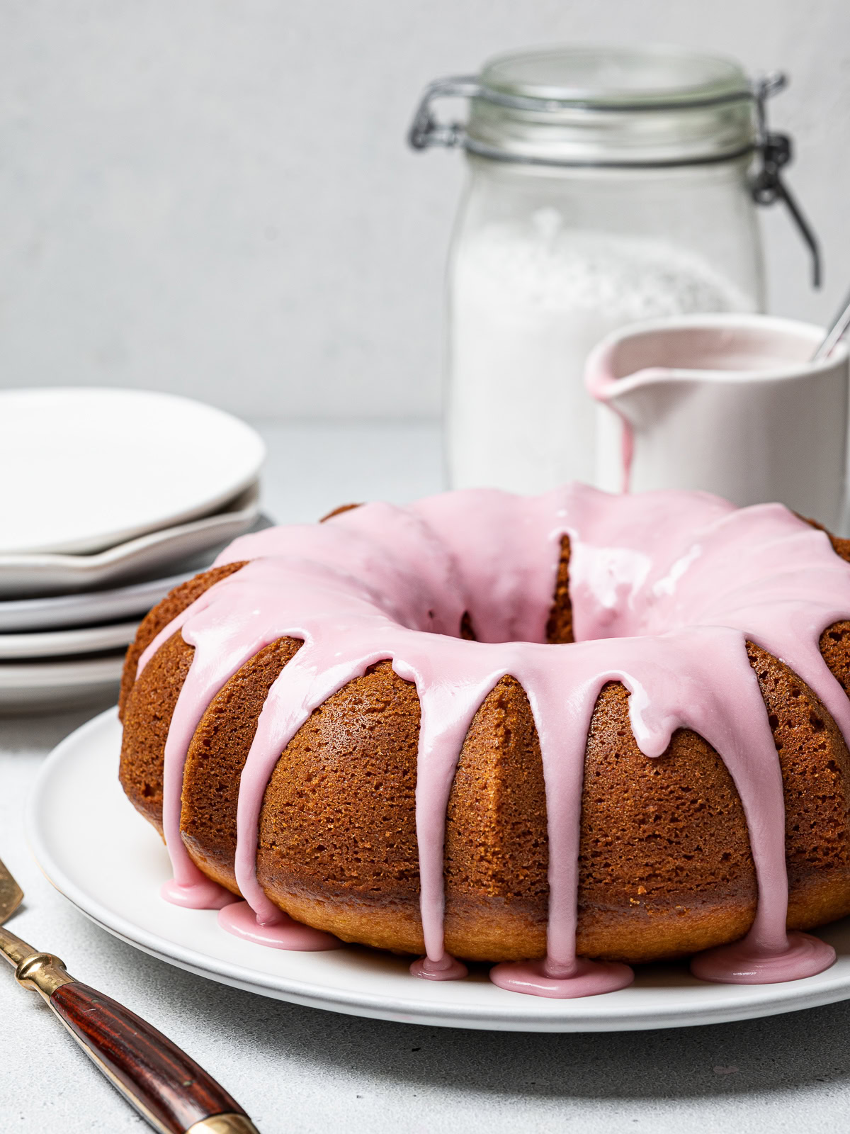 side view of Bundt Cake with blood orange glaze, plates and bottles in background