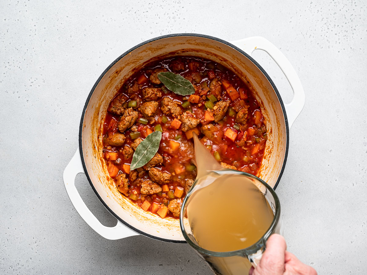 pouring chicken broth into sausage, vegetable, and tomato mixture