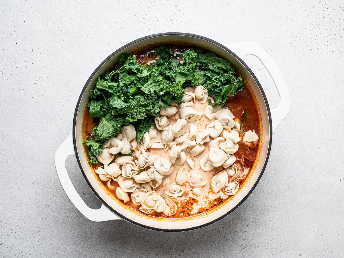 adding tortellini and kale to soup pot