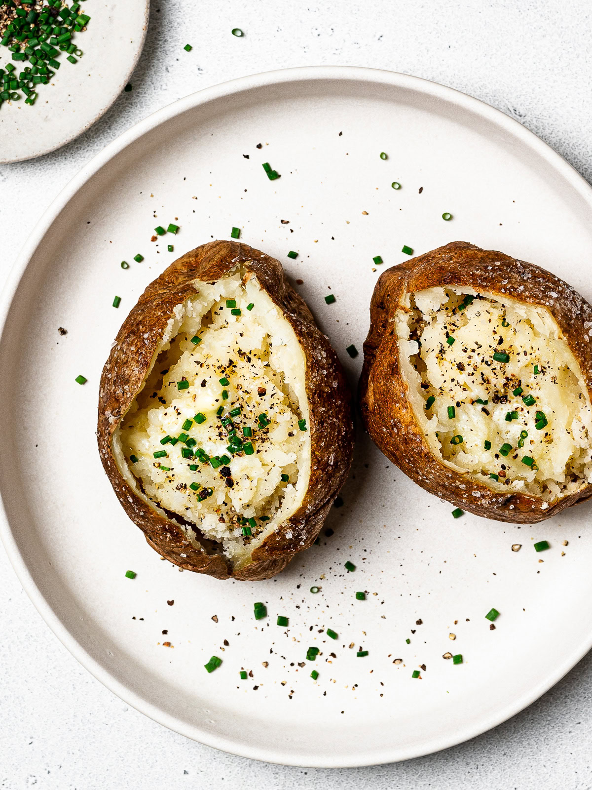 two baked potatoes on a plate topped with butter and chives