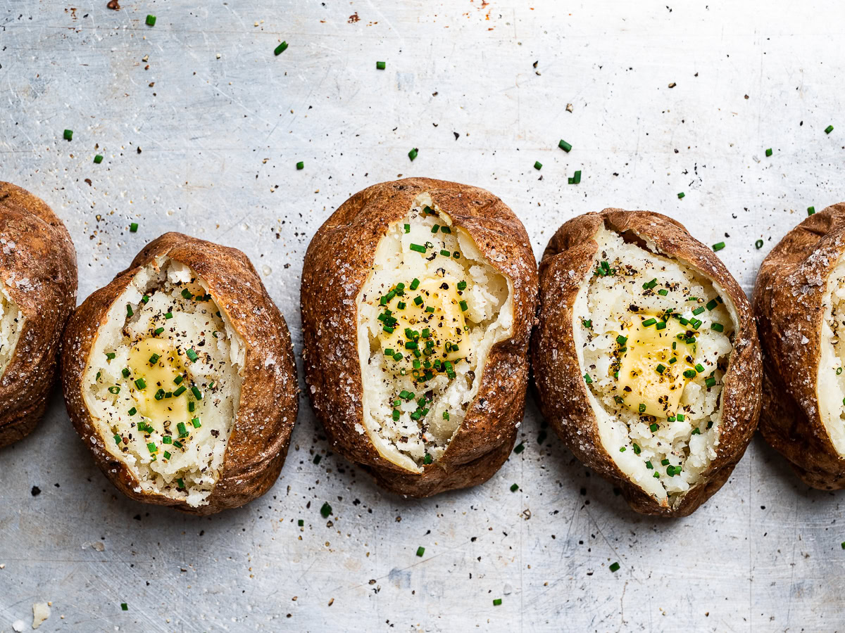 baked potatoes lined up topped with butter and chives