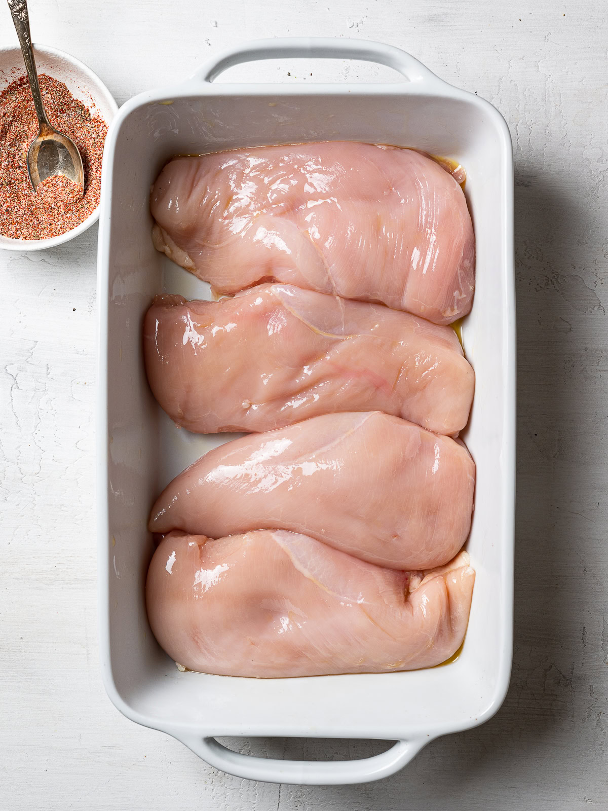 chicken breast in baking dish, bowl of mixed spices on the side