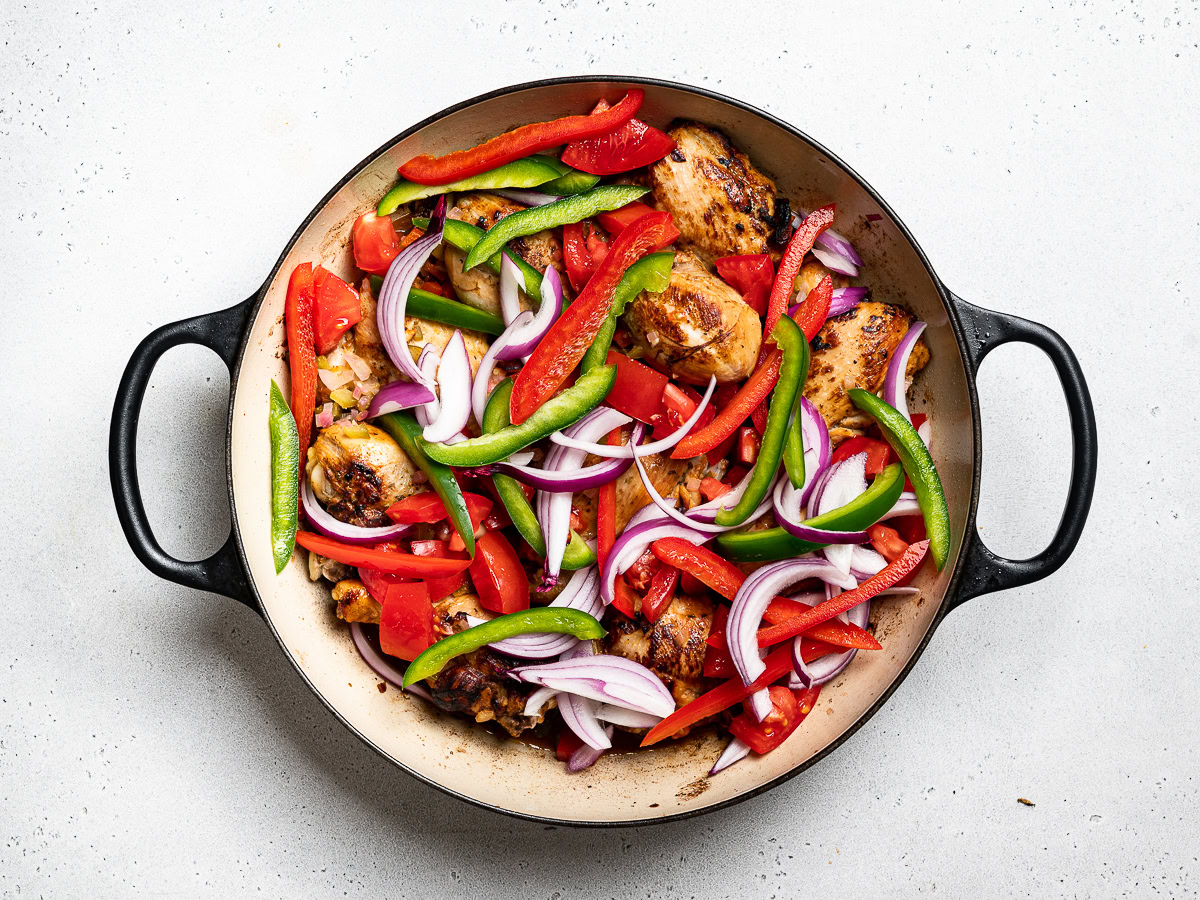 thin slices of peppers and onion added to chicken in skillet