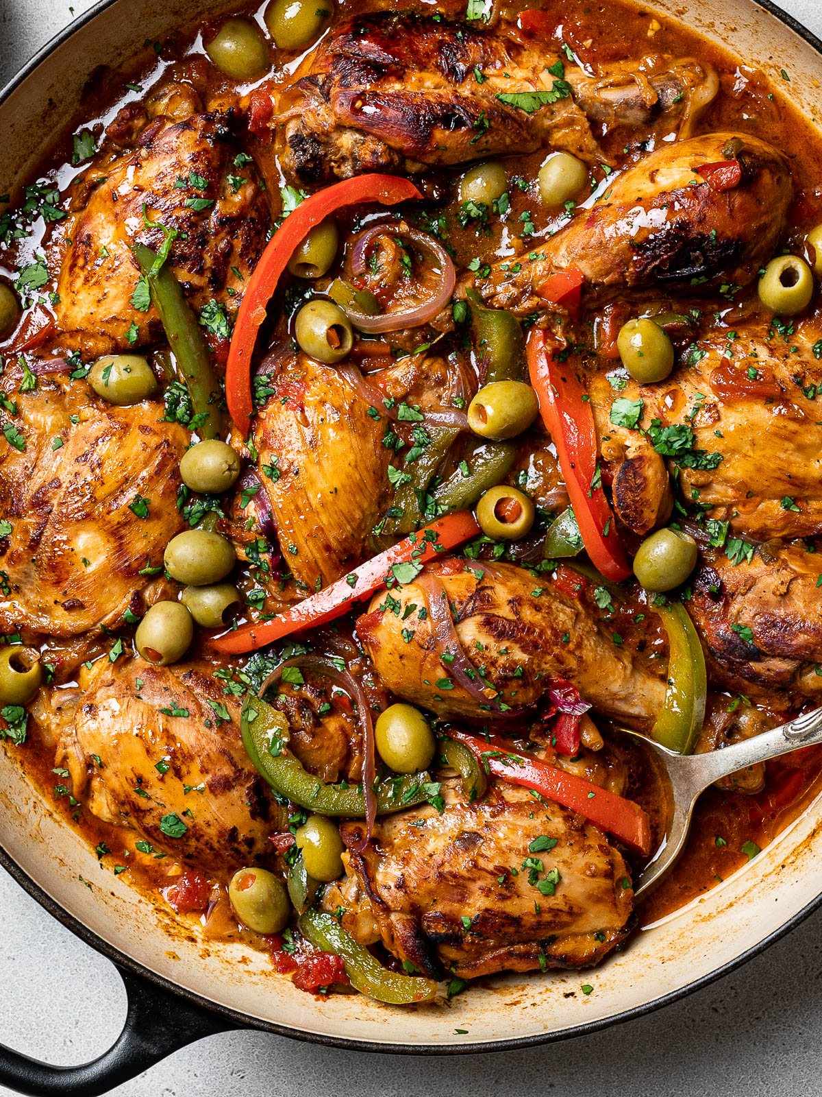 close-up of pollo guisado in skillet; stewed chicken in tomato-based sauce with peppers, and olives 