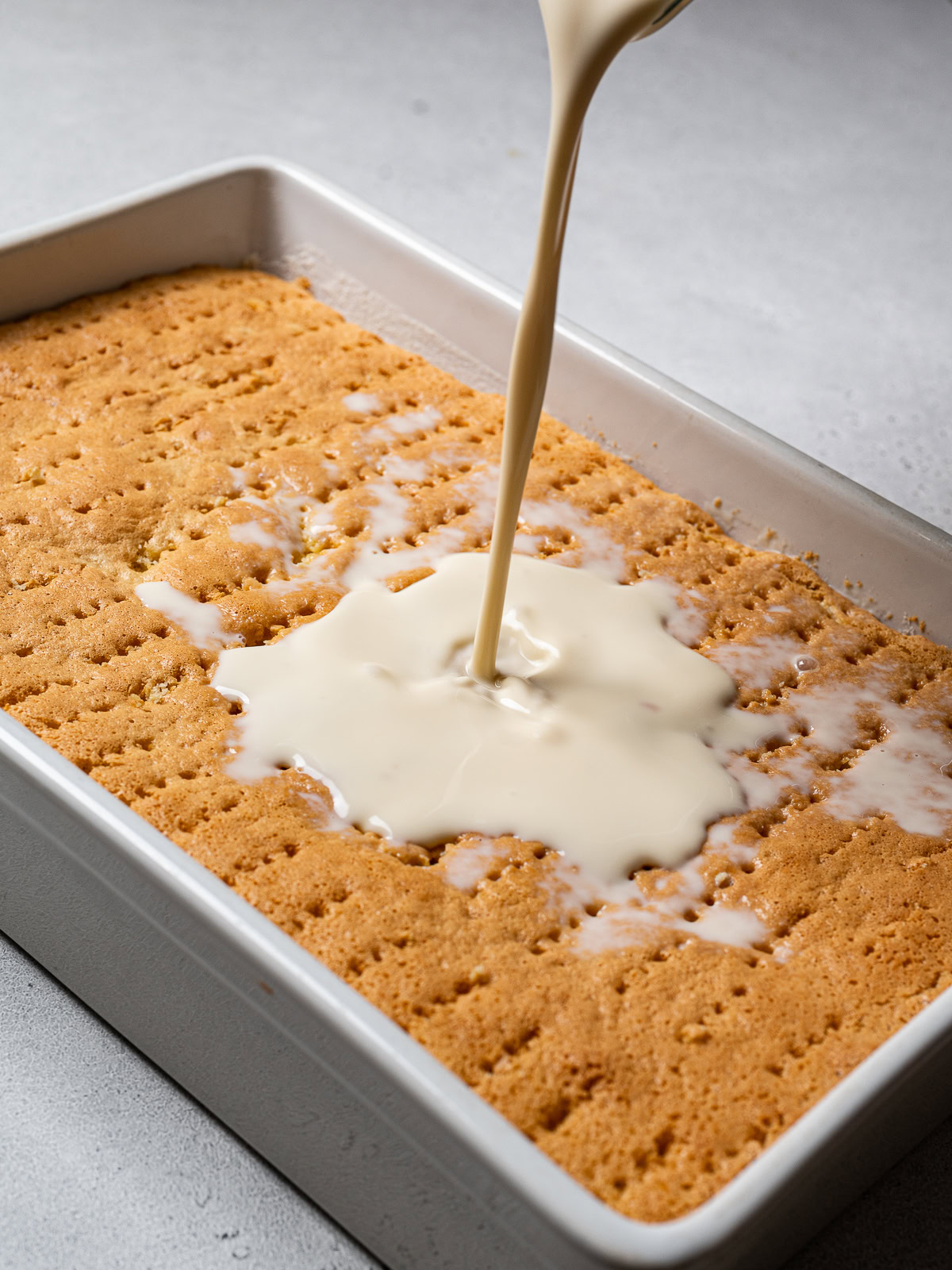 pouring the three milk mixture over the top of the cake