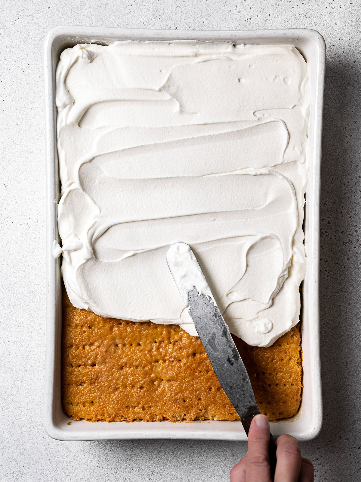 spreading all the whipped cream over top of the cake