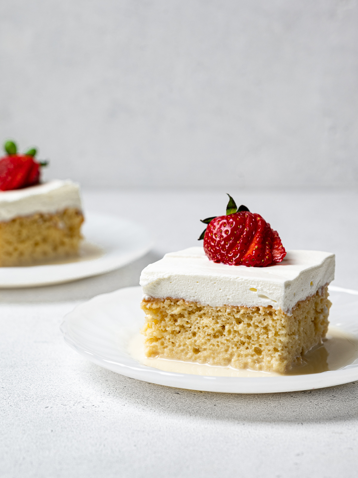 two slices of tres leches cake served on plates and topped with strawberries