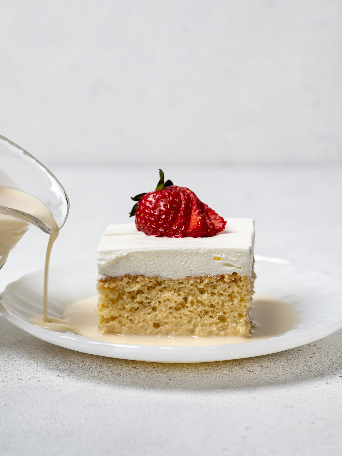 pouring a drizzle of milk syrup onto a plated slice of tres leches cake 