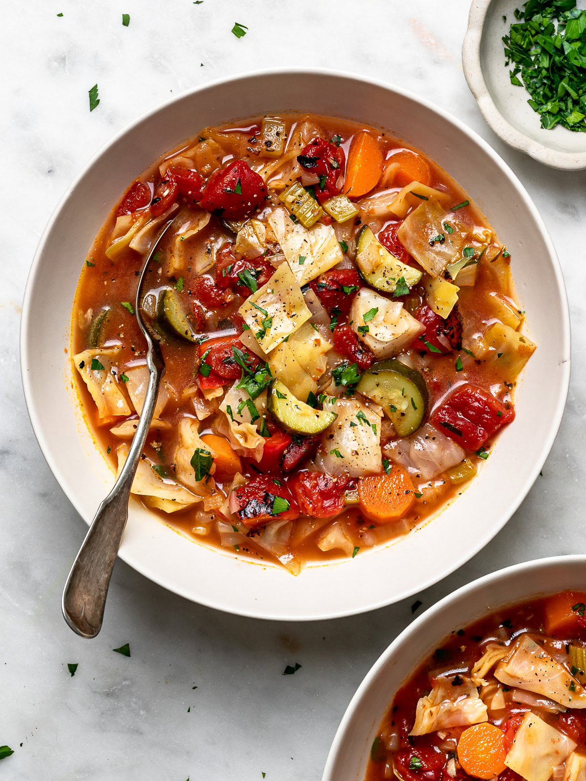 cabbage soup served in two bowls with chopped parsley in a small bowl on the side