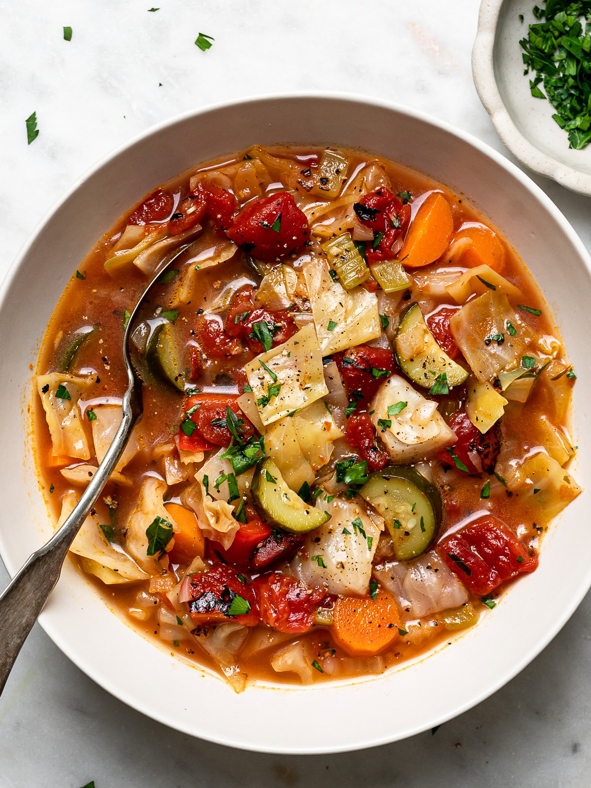 cabbage soup served in one bowl with chopped parsley in a small bowl on the side