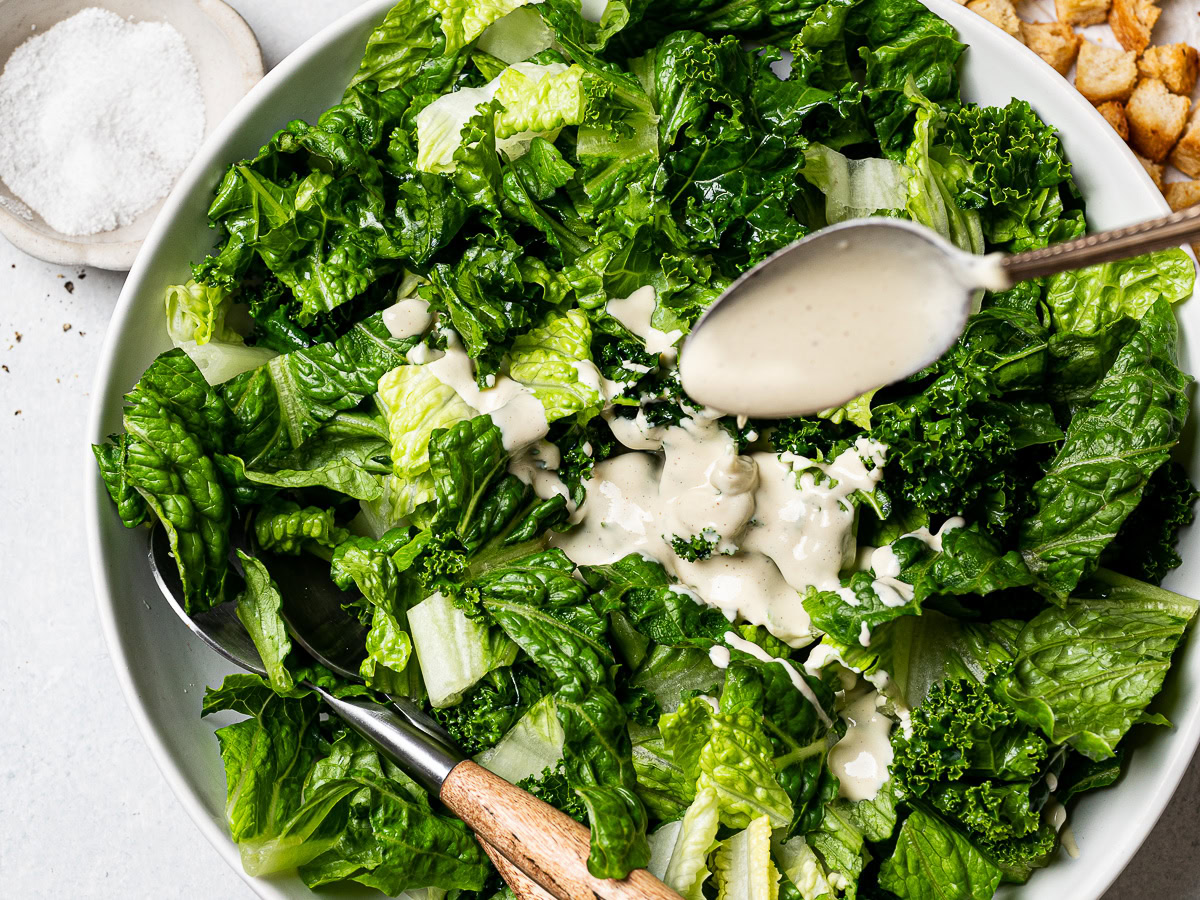 drizzling dressing over chopped kale and romaine leaves