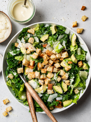kale and romaine Caesar Salad in a bowl topped with croutons, avocado, and shaved parmesan