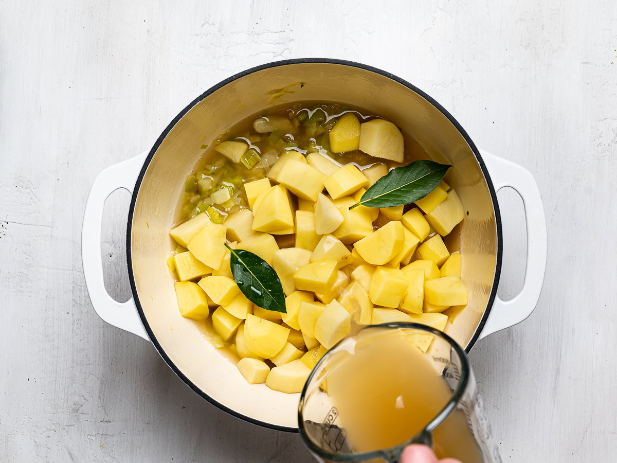 adding broth to potatoes and leeks in soup pot