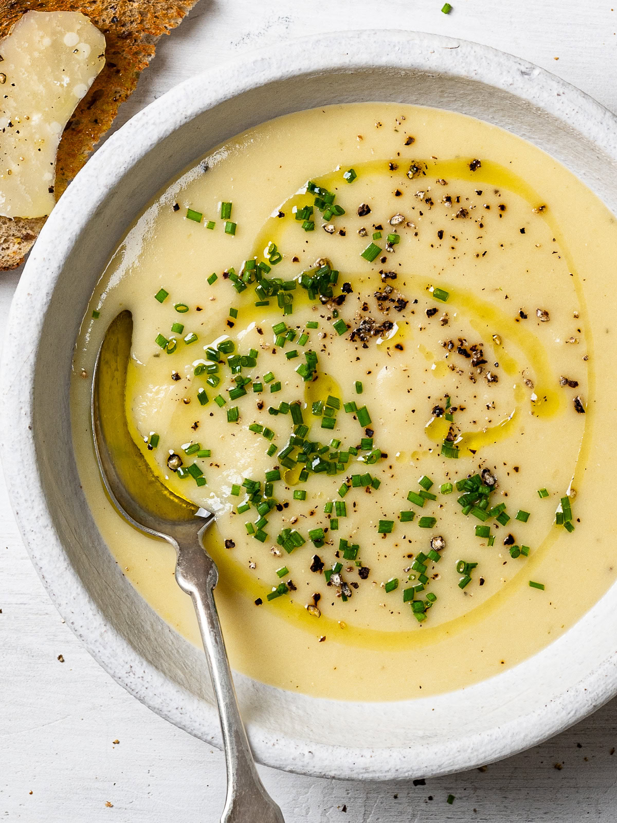 close up of potato leek soup served in individual bowl garnished with chopped chives and freshly cracked black pepper