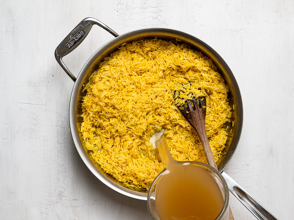 pouring broth into skillet with rice