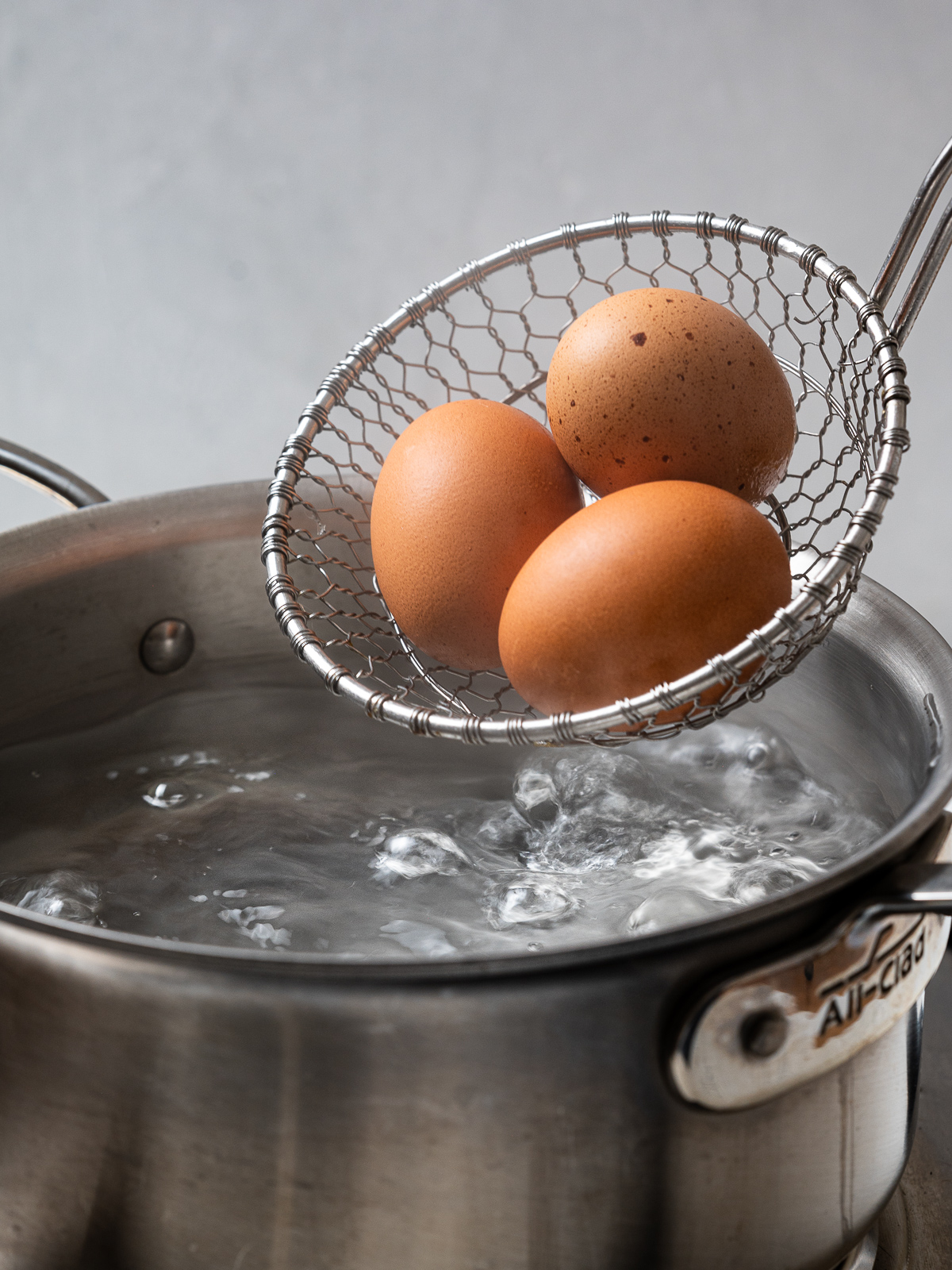 eggs in skimmer about to be lowered into a pot of boiling water