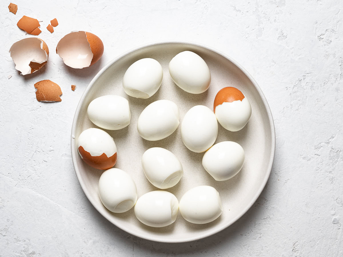 peeled hard boiled eggs on a plate with egg shells beside it 