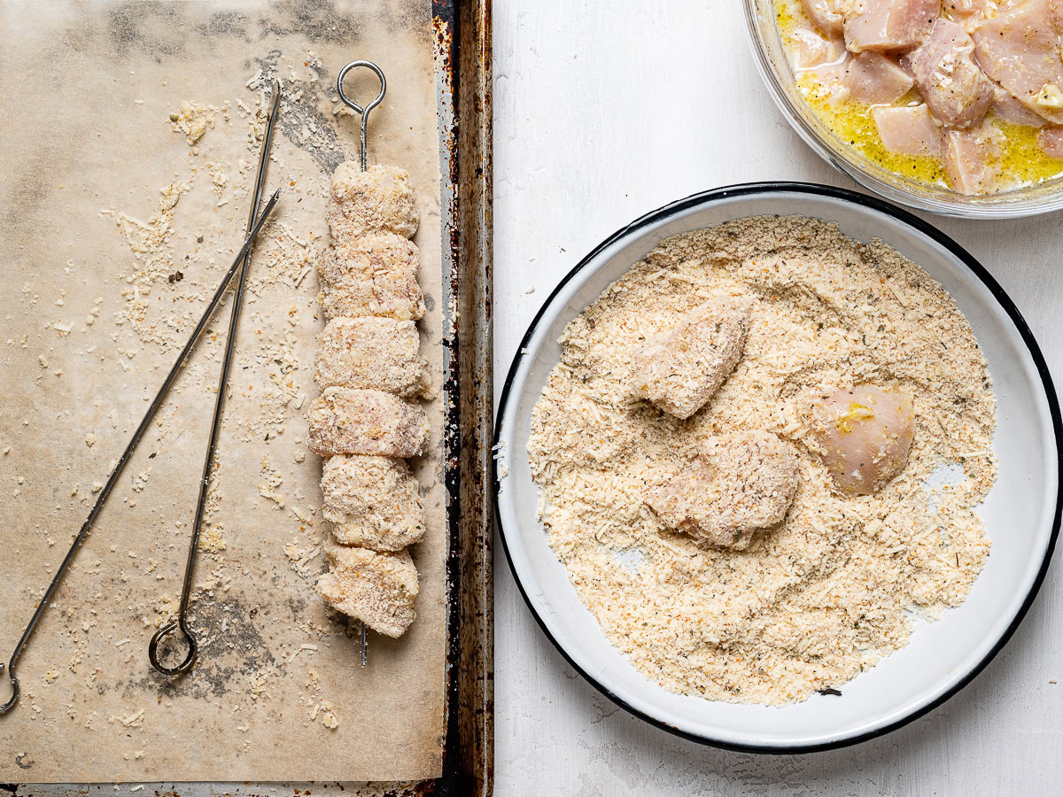 coating chicken cubes in breadcrumbs and threading onto skewers 