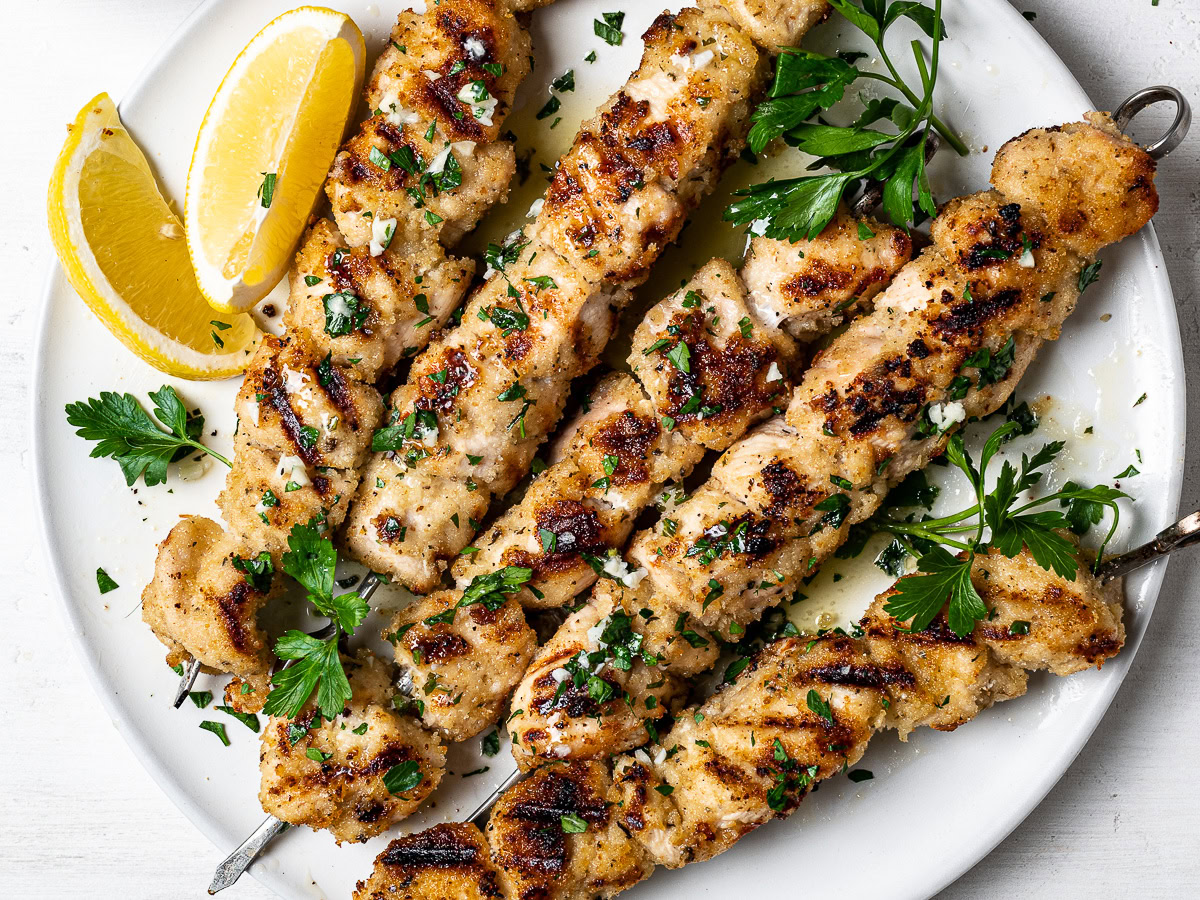 close-up of grilled chicken spiedini skewers served on platter with lemon wedges and lemon butter sauce on the side