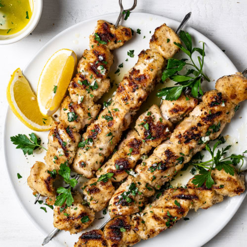 grilled chicken spiedini skewers served on platter with lemon wedges and lemon butter sauce on the side