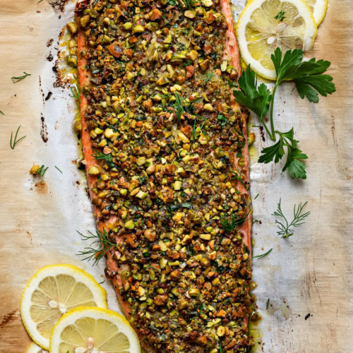 baked pistachio-crusted salmon on baking sheet garnished with dill and lemon slices