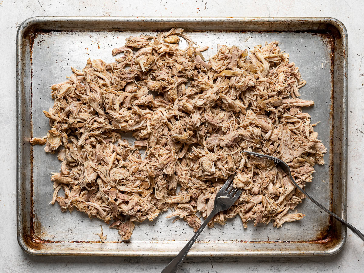 shredding chicken with two forks on sheet pan 