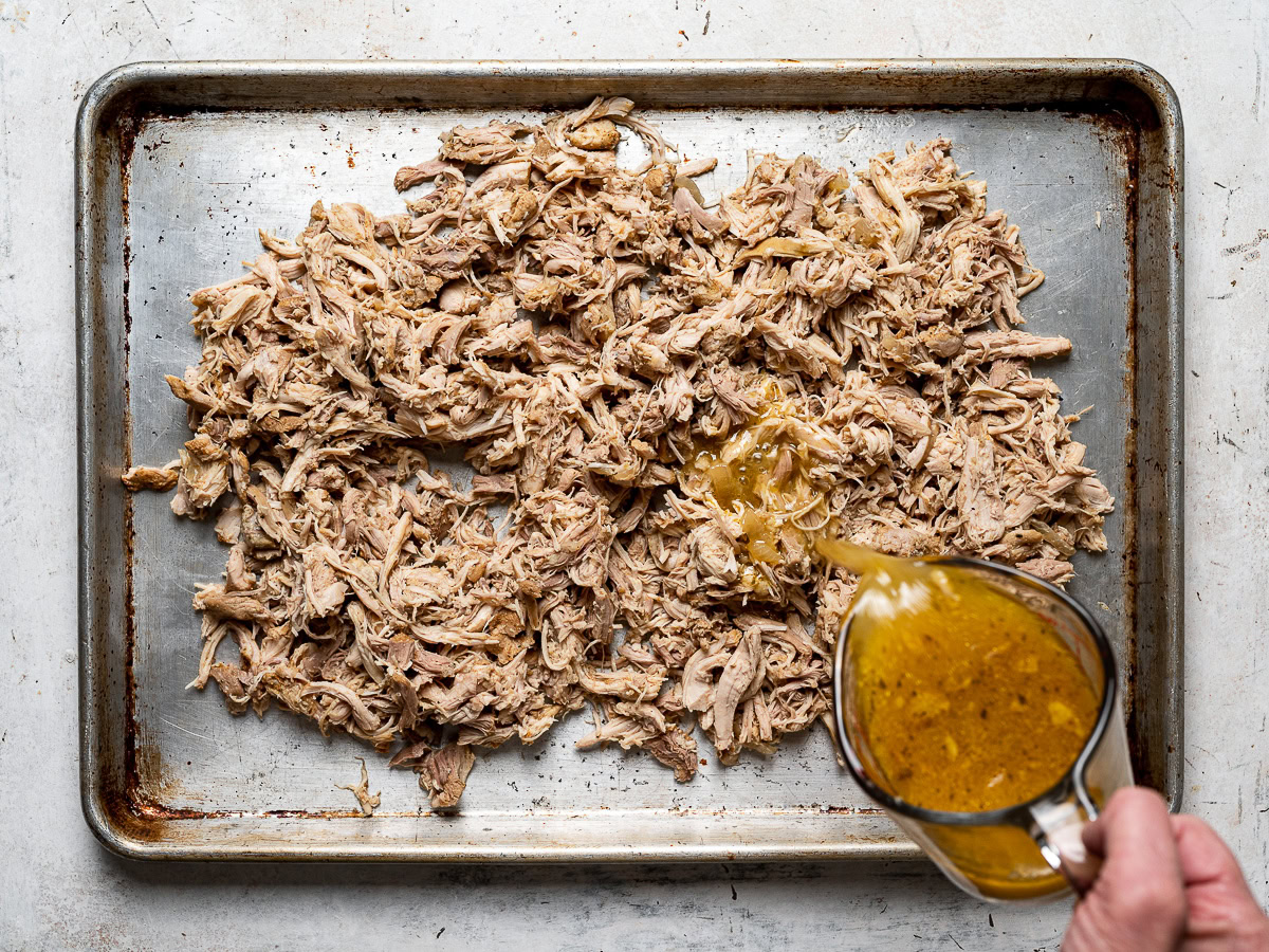 pouring cooking liquid over shredded chicken on sheet pan