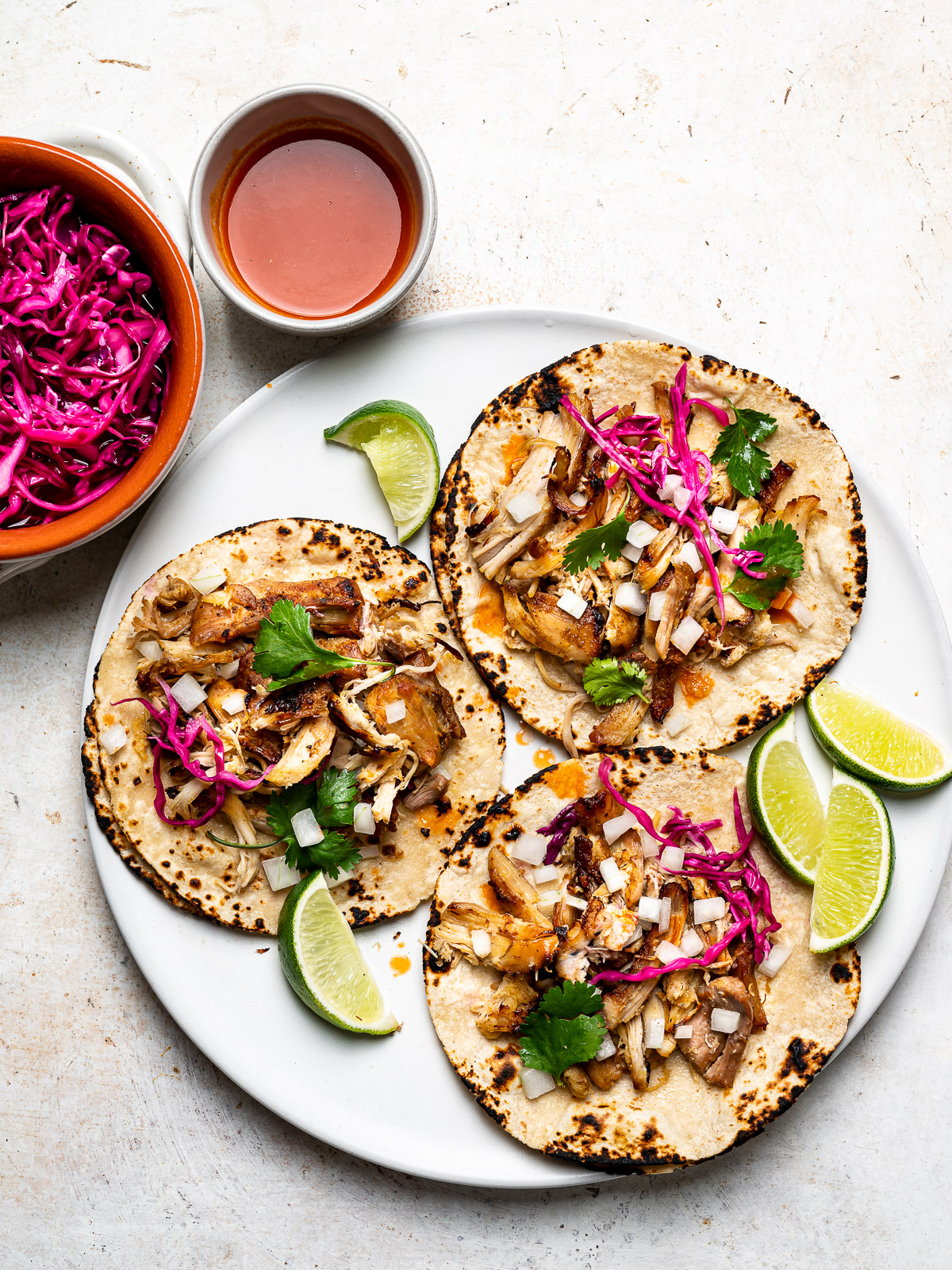 carnitas served on warm corn tortillas topped with onion and pickled red cabbage