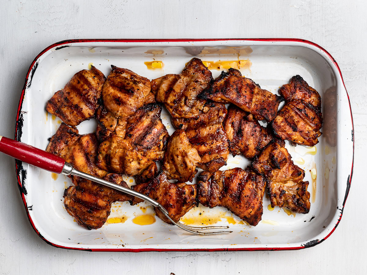 Grilled, slightly charred Peruvian chicken thighs in baking pan.