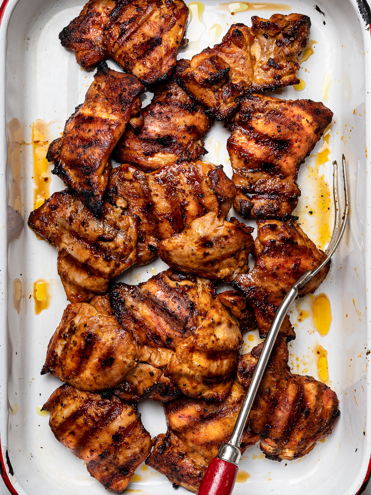 Close up of grilled, slightly charred Peruvian chicken thighs in baking pan. 