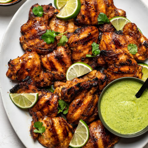 Grilled Peruvian chicken thighs on platter with Aji verde green sauce in a bowl on the side.