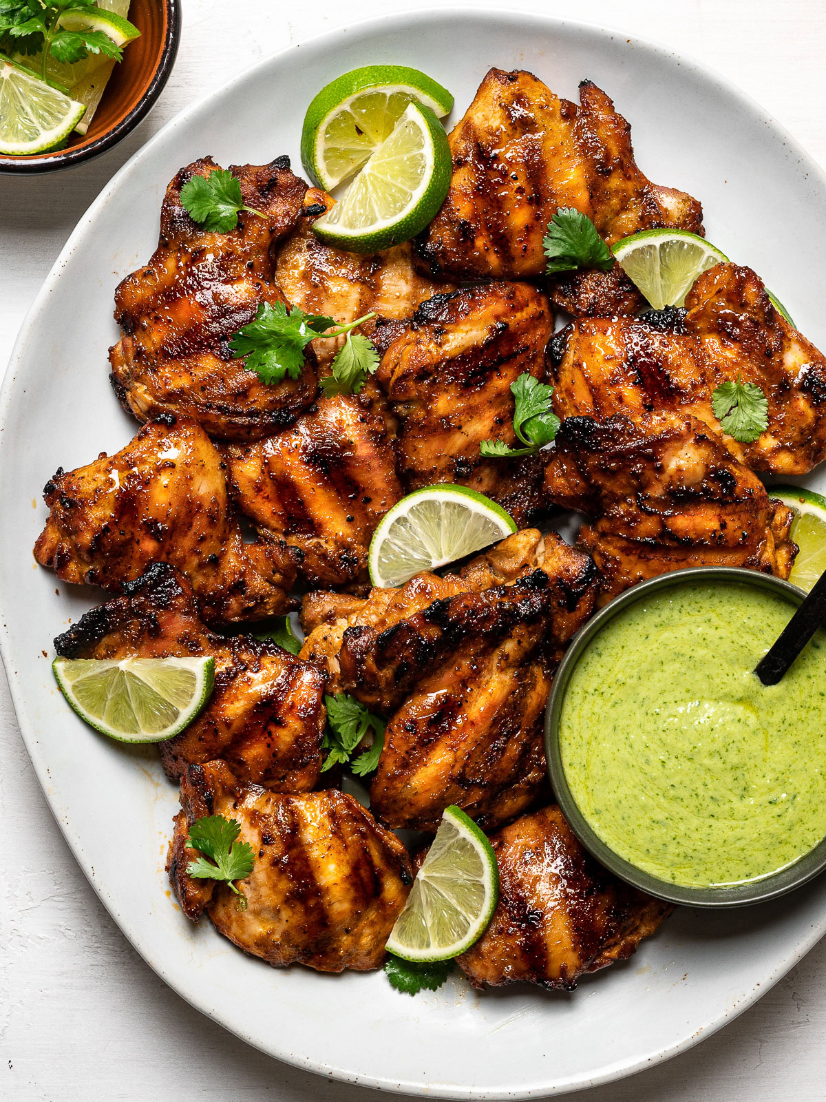 Grilled Peruvian chicken thighs on platter with Aji verde green sauce in a bowl on the side. 