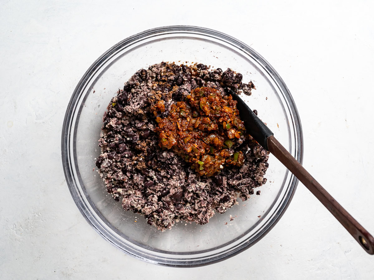 adding onion mixture to mashed beans in bowl