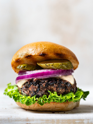 Side view of black bean burger in a bun with lettuce, pickles and sliced red onion